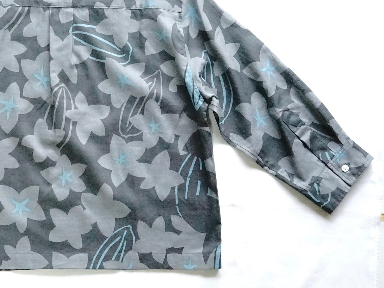 AMONGの花柄シャツ スターフルーツ シルエット 木柄。チャコールにターコイズが映えるスターフルーツの星が印象的。コットン100%が日常に心地よい一枚。